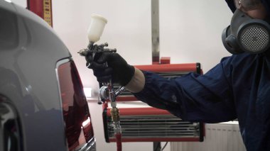 Elinde sprey tabancaları ile çalışan üniforma lı profesyonel ve koruyucu gözlüklü bir solunum cihazı arabanın farklı yerlerine boya (seramik) koyar, elinde bir klasör ile el feneri servis edilebilirlik için bir araba motoru kontrol eder. Kavram 