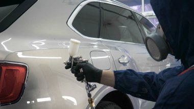 Elinde sprey tabancaları ile çalışan üniforma lı profesyonel ve koruyucu gözlüklü bir solunum cihazı arabanın farklı yerlerine boya (seramik) koyar, elinde bir klasör ile el feneri servis edilebilirlik için bir araba motoru kontrol eder. Kavram 