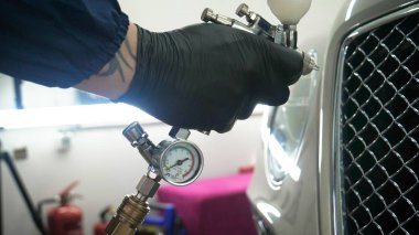 Elinde sprey tabancaları ile çalışan üniforma lı profesyonel ve koruyucu gözlüklü bir solunum cihazı arabanın farklı yerlerine boya (seramik) koyar, elinde bir klasör ile el feneri servis edilebilirlik için bir araba motoru kontrol eder. Kavram 