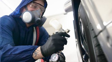 Elinde sprey tabancaları ile çalışan üniforma lı profesyonel ve koruyucu gözlüklü bir solunum cihazı arabanın farklı yerlerine boya (seramik) koyar, elinde bir klasör ile el feneri servis edilebilirlik için bir araba motoru kontrol eder. Kavram 