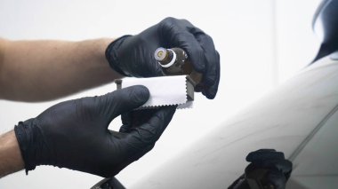 Elinde sprey tabancaları ile çalışan üniforma lı profesyonel ve koruyucu gözlüklü bir solunum cihazı arabanın farklı yerlerine boya (seramik) koyar, elinde bir klasör ile el feneri servis edilebilirlik için bir araba motoru kontrol eder. Kavram 