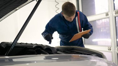 Elinde sprey tabancaları ile çalışan üniforma lı profesyonel ve koruyucu gözlüklü bir solunum cihazı arabanın farklı yerlerine boya (seramik) koyar, elinde bir klasör ile el feneri servis edilebilirlik için bir araba motoru kontrol eder. Kavram 