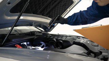 Elinde sprey tabancaları ile çalışan üniforma lı profesyonel ve koruyucu gözlüklü bir solunum cihazı arabanın farklı yerlerine boya (seramik) koyar, elinde bir klasör ile el feneri servis edilebilirlik için bir araba motoru kontrol eder. Kavram 