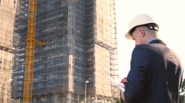 Oluşturucu veya mühendis, duruyor onun binaları, seyir sırt ile beyaz bir miğfer ve Evet, bir gökdelen bir takım elbise