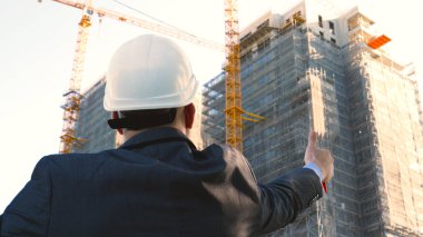 Oluşturucu veya mühendis, duruyor onun binaları, seyir sırt ile beyaz bir miğfer ve Evet, bir gökdelen bir takım elbise