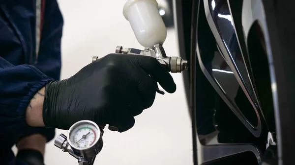 Professional in working uniform with spray guns in his hands and a respirator in protective glasses puts paint (ceramics) on the car on different parts of the car, flashlight with a folder in his hands checks a car engine for serviceability. Concept