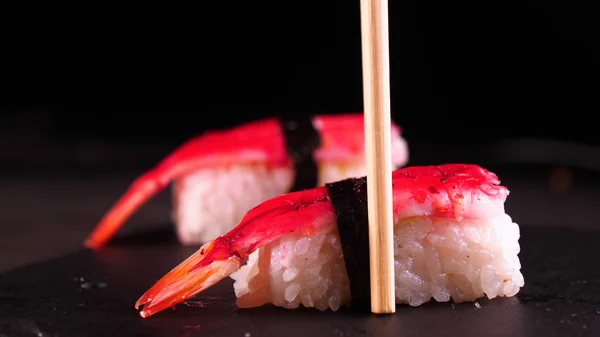 On a dark background on a tray, cooked or purchased sushi (Nigiri) taste Chinese chopsticks. Concept of: Nigiri, Sushi of the Day, Two, Tasty, Sticks, Very Close, Slow Motion.