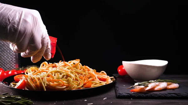 Cooked dish at home (in a restaurant) chef opens (removes) the lid from the pan. It can be seen in her pasta (noodles) differently colored,the chef decorates the finished pasta dish with grated Parmesan cheese on a kitchen grater and adding the sauce
