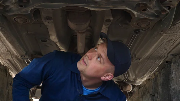 A cheerful car repairman on the street repairs the engine and lower part of the car, shows different emotions, dances with a big wrench. Concept of: Service, Joy, Slow motion, Mood, Happy, Repair.