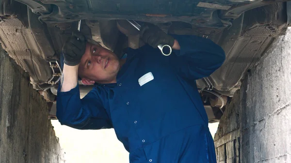 A cheerful car repairman on the street repairs the engine and lower part of the car, shows different emotions, dances with a big wrench. Concept of: Service, Joy, Slow motion, Mood, Happy, Repair.