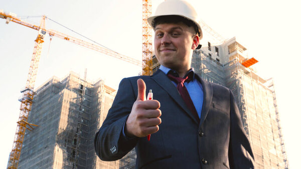 Builder or engineer, stands with his back looking at the buildings, wearing a white helmet and wearing a suit, talking on the phone, a skyscraper