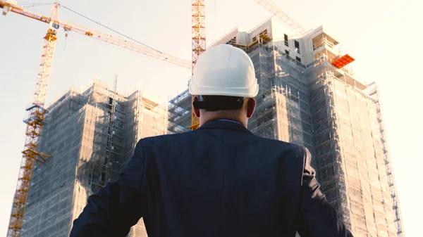 Oluşturucu veya mühendis, duruyor onun binaları, seyir sırt ile beyaz bir miğfer ve Evet, bir gökdelen bir takım elbise