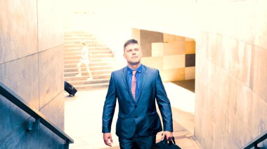 Takım elbiseli genç yakışıklı işadamı elinde siyah bir çantayla merdivenlerden çıkıyor. Konsept: iş, takım, adam, adam, çanta, iş adamı.