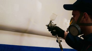 Genç adam (adam) garajda yatı parlatan beyaz önlüklü bir uzman. Hazırlık, Temizlik, Parlatma, Master, Profesyonellik, Boyamadan sonra, Kimya Kullanımı.