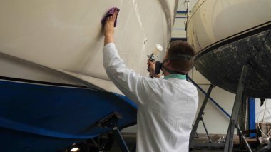 Genç adam (adam) garajda yatı parlatan beyaz önlüklü bir uzman. Hazırlık, Temizlik, Parlatma, Master, Profesyonellik, Boyamadan sonra, Kimya Kullanımı.