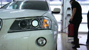 Profesyonel adam (adam) bir araba yıkama Karcher kullanarak çok kirli bir araba yıkar ve köpük sıçramaları, bir sünger ile araba siler. Konsept: Oto yıkama, yıkama aksesuarları, yüksek basınç altında.