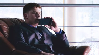 Bir adam pencerenin yanında binada elinde bir cep telefonu tutar,İki genç erkek (çocuklar), işadamları, el sıkışma, bir binada bir toplantıda birbirlerine selamlama (ofis) Kavramı: İş toplantısı, Çok Yakın, Önemli Meet