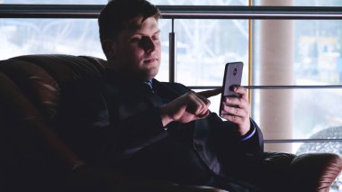 Bir adam pencerenin yanında binada elinde bir cep telefonu tutar,İki genç erkek (çocuklar), işadamları, el sıkışma, bir binada bir toplantıda birbirlerine selamlama (ofis) Kavramı: İş toplantısı, Çok Yakın, Önemli Meet