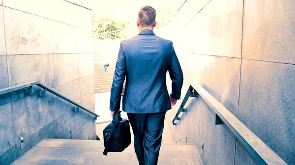Young handsome guy businessman in a suit, (man) climbs the stairs with a black bag in his hands. Concept: business, suit, guy, man, bag, businessman.
