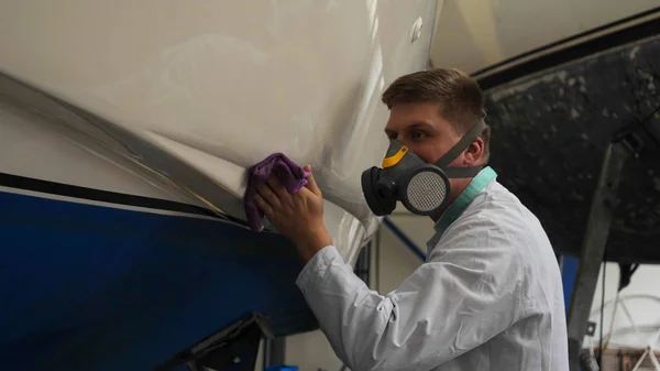 Genç adam (adam) garajda yatı parlatan beyaz önlüklü bir uzman. Hazırlık, Temizlik, Parlatma, Master, Profesyonellik, Boyamadan sonra, Kimya Kullanımı.