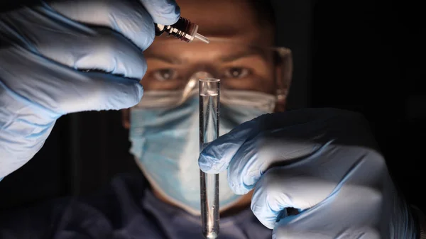 一名男性实验室技术员 一个戴着实验室眼镜的科学工作者 看着试管 非常仔细地滴血 穿着工作制服的男医生戴着手套 戴着护目镜检查体外分析 — 图库照片