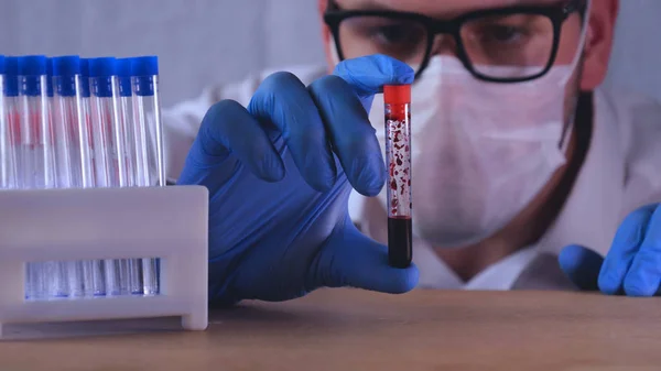 Laboratory work, the doctor holds a syringe, in a medical mask and glasses, takes a test from a test tube in blue rubber gloves, analysis, blood, DNA, a test tube holder.
