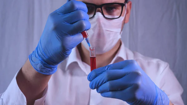 Laboratory work, the doctor holds a syringe, in a medical mask and glasses, takes a test from a test tube in blue rubber gloves, analysis, blood, DNA, a test tube holder.