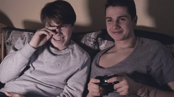 Two friends (guys) play video game console, have fun, laugh, hold the joystick.