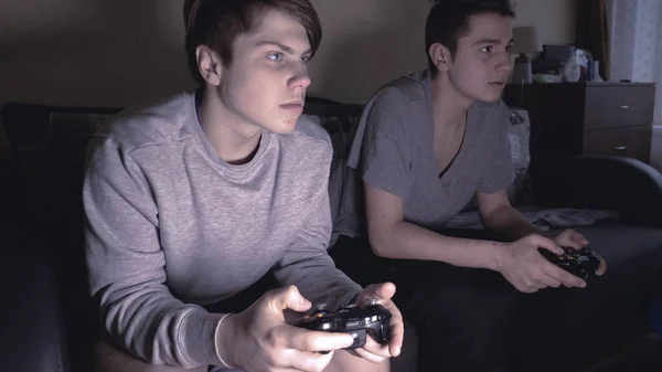 Two friends (guys) play video game console, have fun, laugh, hold the joystick.