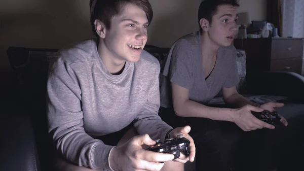 Two friends (guys) play video game console, have fun, laugh, hold the joystick.