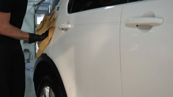 Профессиональный автомойщик стирает и сушит окно после мойки автомобиля. Концепция от: Очки для чтения, Профессиональная работа, Черные перчатки, Голубая тряпка
