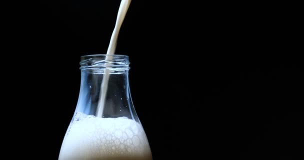 Mléko v pomalém pohybu nalijte do lahve, mléko ve skleněné láhvi umístěné na potahu. Koncept: čerstvé, nalít, černé pozadí.
