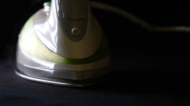 Demir, siyah bir arka planda çok yakındır. Ütü bezi (gömlek) siyahtır; Buhar bir sürü demir çıkıyor. Kavramı: Buhar, Close, siyah.