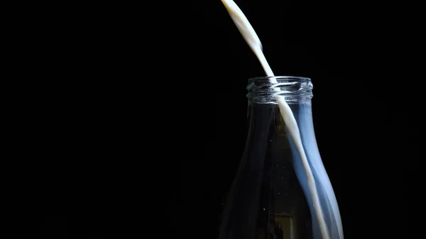 ゆっくりした動きでボトルに牛乳を注ぎ ガラス瓶の牛乳を袋の上に置きます コンセプト フレッシュ 黒の背景 — ストック写真