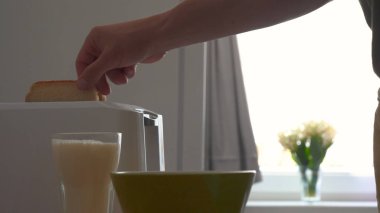 Mutfakta, bir erkek (kız) buzdolabından yiyecek çıkarır ve tost makinesinin yanına kahvaltı hazırlar, hazır ekmek kızartma makineleri çıkarılır. Ev yapımı yemek, rahatlık, kahvaltı, ağır çekim kavramı.