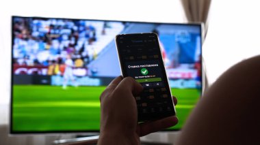 Evde TV arka plan (barda) karşı, adam (kadın) farklı atıştırmalıklar, pizza ve tatlılar cep telefonları kullanarak internet mağazaları üzerinden kaydırma sipariş. Konsept: futbol, spor, sipariş.
