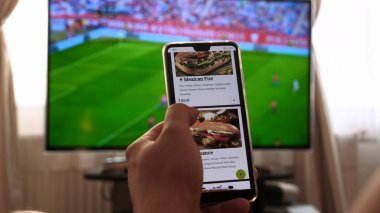 Evde TV arka plan (barda) karşı, adam (kadın) farklı atıştırmalıklar, pizza ve tatlılar cep telefonları kullanarak internet mağazaları üzerinden kaydırma sipariş. Konsept: futbol, spor, sipariş.
