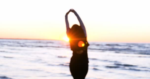 一个年轻的女人在日落的背景下 在海滨晒太阳 做运动 伸展和滑行 海上的女孩做瑜伽 慢动作 日落的肖像 — 图库视频影像