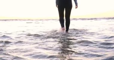 Günbatımının arka planında genç bir kadın deniz kıyısında güneş egzersizlerini koşarak, gerinerek ve düşerek yapar, denizdeki kız yoga yapar. Yavaş çekim, Günbatımı 'nın Portresi.