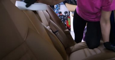 Araba yıkamacıdaki bir kadın özel kimya, giysi, sünger ve fırça kullanarak arabanın tüm parçalarını kuru temizlemeye verir. Tam araba temizliği, kuru temizleme, profesyonel hizmet. Araba, iş.