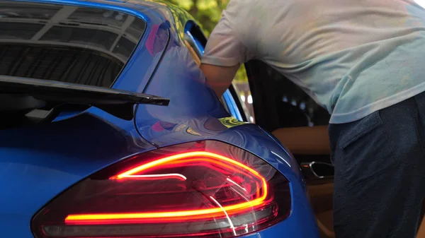 A man in the garage (Service) salon puts his bag in the salon (in the trunk), checking and turning off the car alarm. A man opens the door and trunk in a new car. Concept of: Slow mo, Car shop, Man.