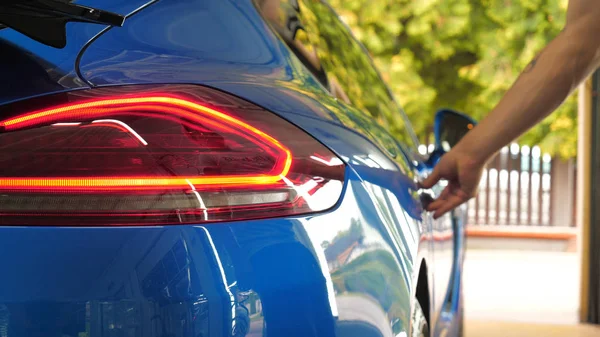 A man in the garage (Service) salon puts his bag in the salon (in the trunk), checking and turning off the car alarm. A man opens the door and trunk in a new car. Concept of: Slow mo, Car shop, Man.