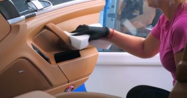 Araba yıkamacıdaki bir kadın özel kimya, giysi, sünger ve fırça kullanarak arabanın tüm parçalarını kuru temizlemeye verir. Tam araba temizliği, kuru temizleme, profesyonel hizmet. Araba, iş.