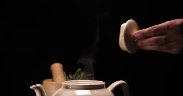 在黑色背景下 托盘上的煮过的茶壶 是柠檬和青草茶托 从茶壶里冒出大量的水汽 露出被压碎的痕迹 热水灌满 茶壶里的茶杯里有茶 — 图库视频影像