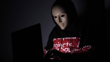 Erkek hacker karanlıkta dizüstü bilgisayar (telefon) kişisel bilgilere erişen maske ile gizli yüz. Teknoloji, siber suç kavramı. 