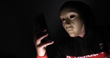 Erkek hacker karanlıkta dizüstü bilgisayar (telefon) kişisel bilgilere erişen maske ile gizli yüz. Teknoloji, siber suç kavramı. 