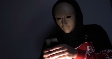 Erkek hacker karanlıkta dizüstü bilgisayar (telefon) kişisel bilgilere erişen maske ile gizli yüz. Teknoloji, siber suç kavramı. 