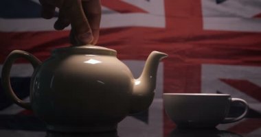 İngiliz bayrağının arka planında İngiliz çayıyla demlenmiş çay ve dumanlı bir bardağa dökülmüş. İngiliz Çay, Yavaş Hareket, Bayrak, Gerçek Çay Konsepti.