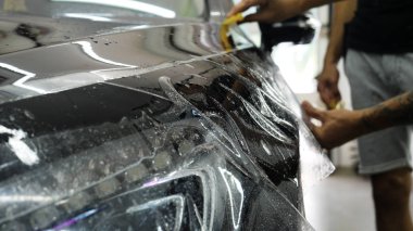 Ön far ve kaputta Ppf montaj işlemine yakın. Ppf, boyayı çizilmelerden ve taş yongalarından koruyan bir Boya Koruma Filmidir. Konsept: Koruma, Koruma, Araba, Yeni, İş.