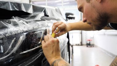 Ön far ve kaputta Ppf montaj işlemine yakın. Ppf, boyayı çizilmelerden ve taş yongalarından koruyan bir Boya Koruma Filmidir. Konsept: Koruma, Koruma, Araba, Yeni, İş.